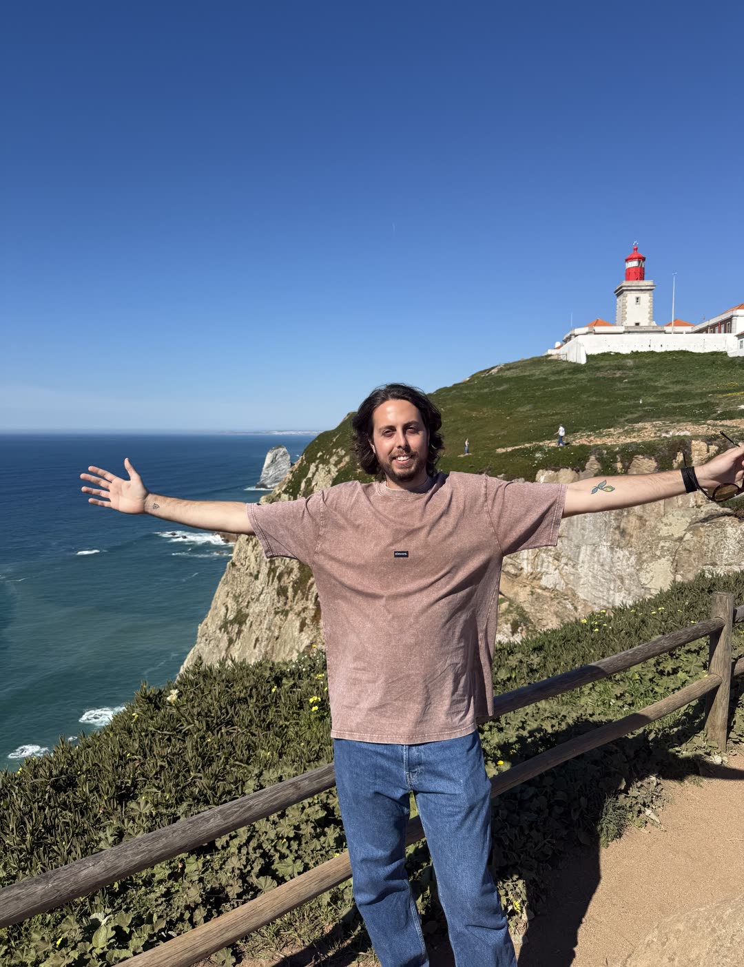 Simone on a clifftop above the Atlantic, arms open, a lighthouse behind
